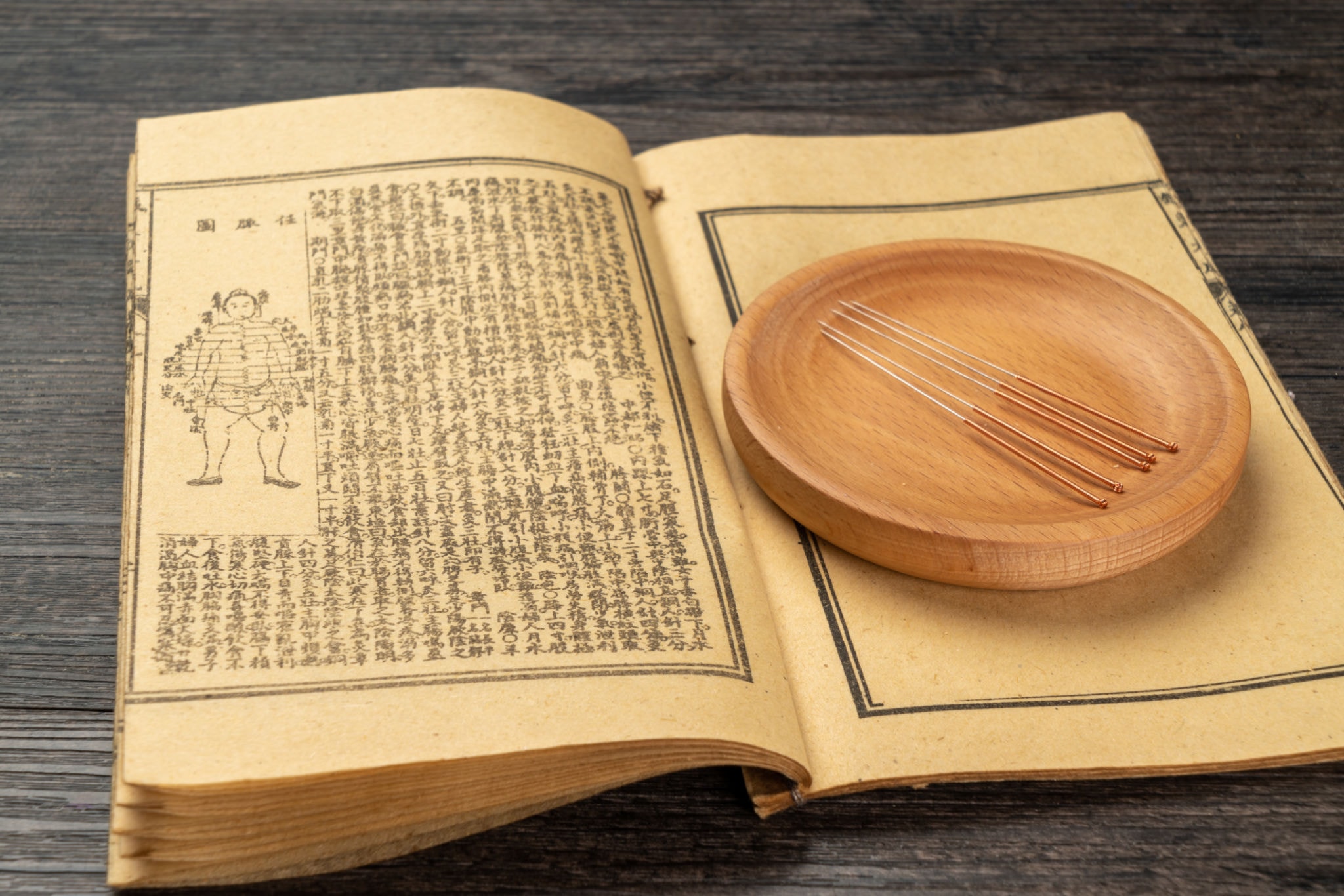 Ancient Chinese acupuncture text with acupuncture needles on a wooden plate